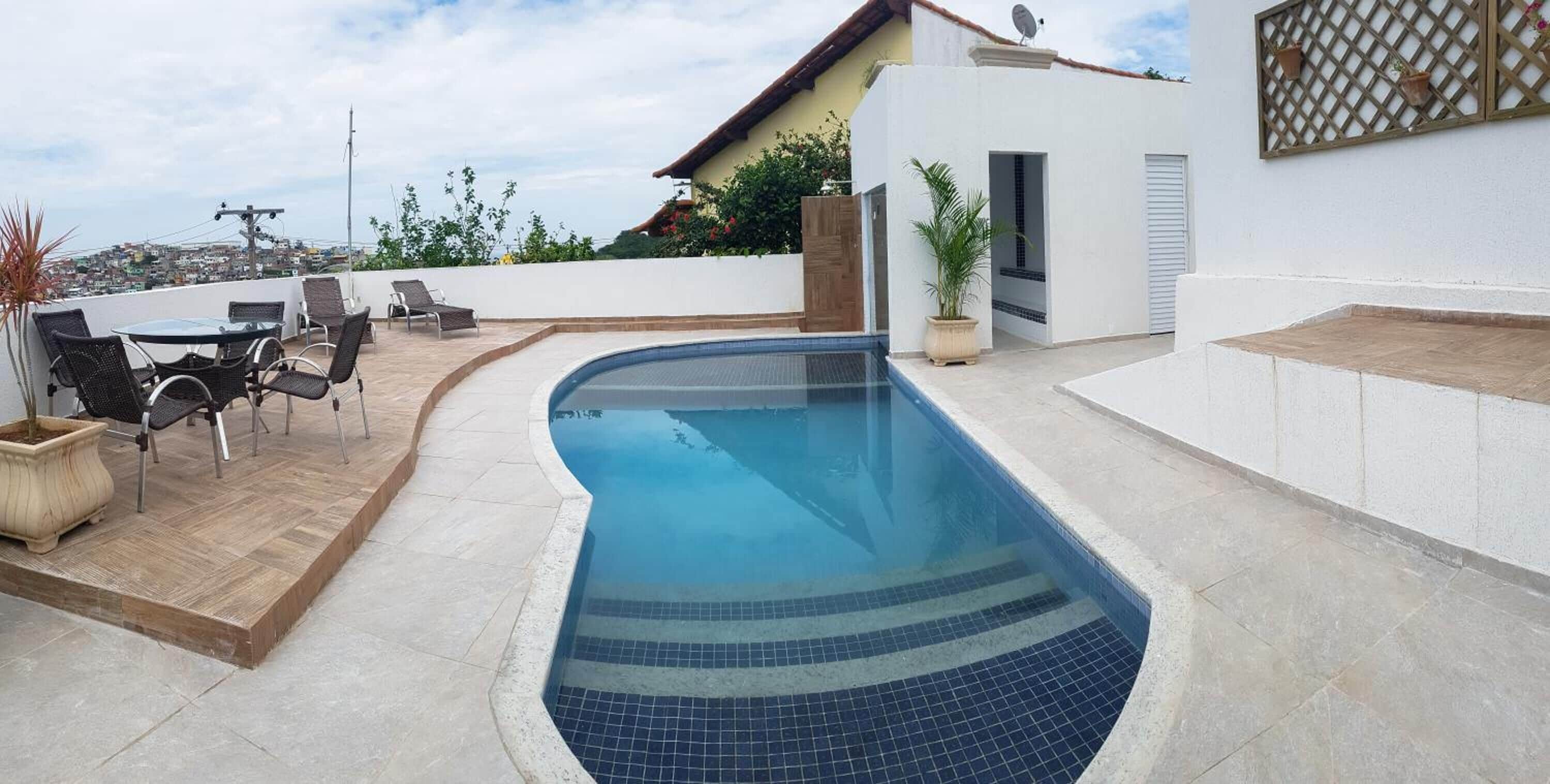 Piscina com borda azulejada, rodeada por um terraço com cadeiras e uma mesa.