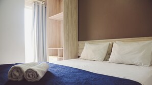 A neatly made bed with a blue blanket and rolled towels, a wooden headboard, and a view of a wooden wardrobe. - Pousada Xerxes (Arraial do Cabo)