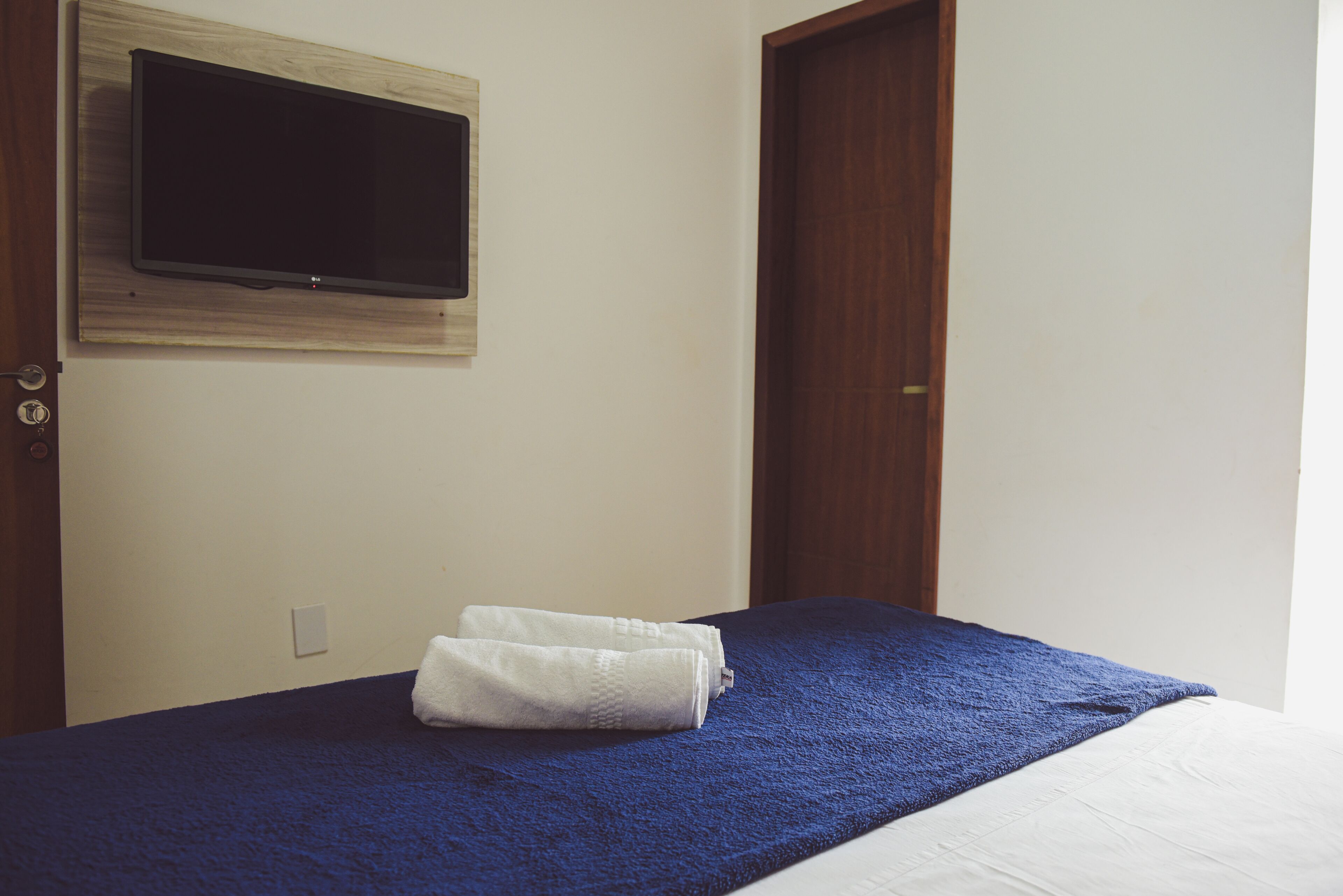 Une chambre d’hôtel avec un lit, un téléviseur à écran plat fixé au mur et une porte en bois.