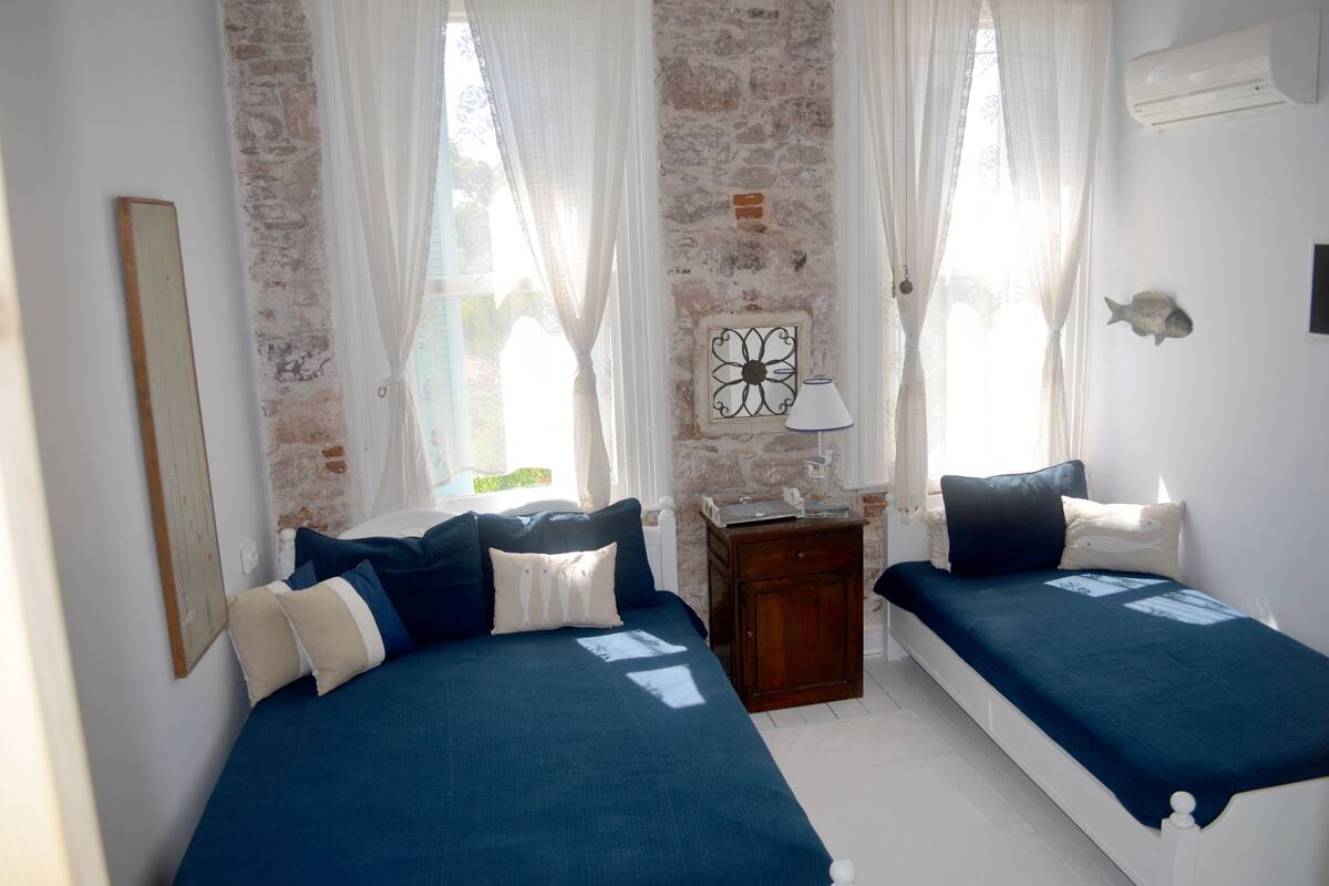 Una habitación con dos camas, una mesita y aire acondicionado instalado en la pared.