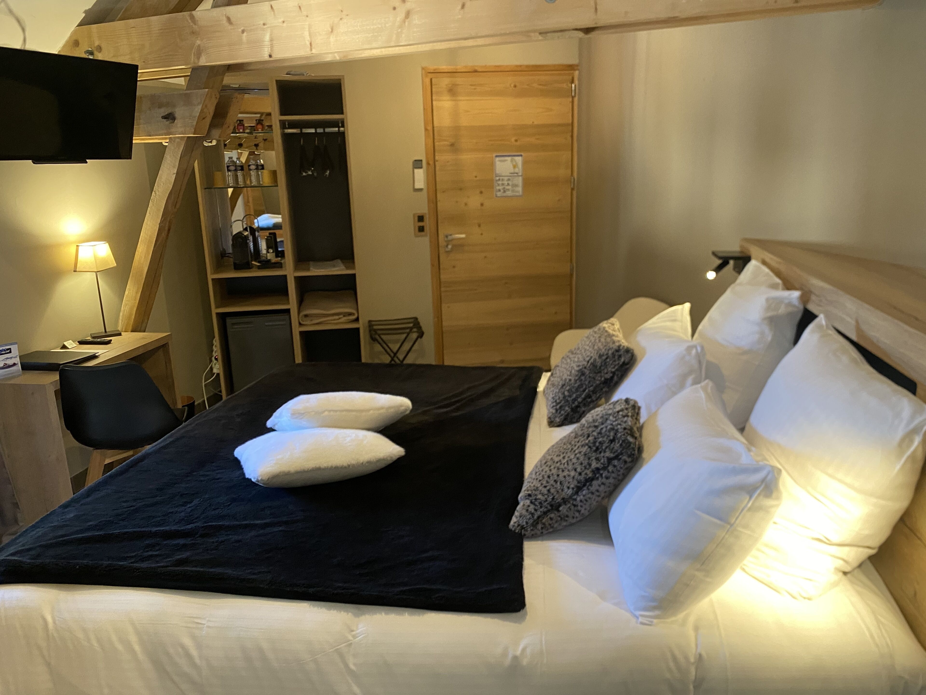 A hotel room with a bed, a desk, a chair, a TV, and a wooden wardrobe.