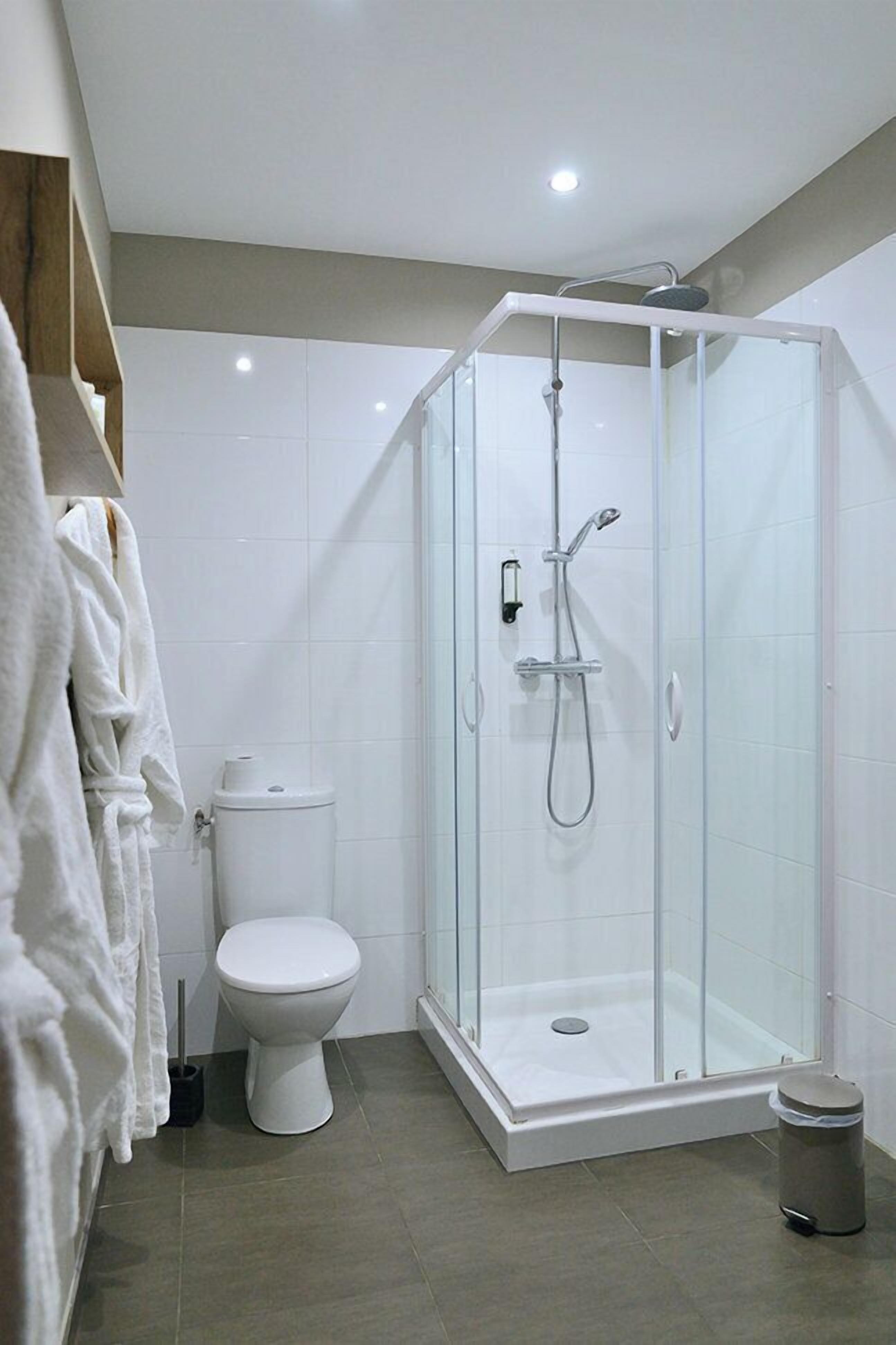 A modern bathroom with a glass-enclosed shower, a toilet, and a trash bin.
