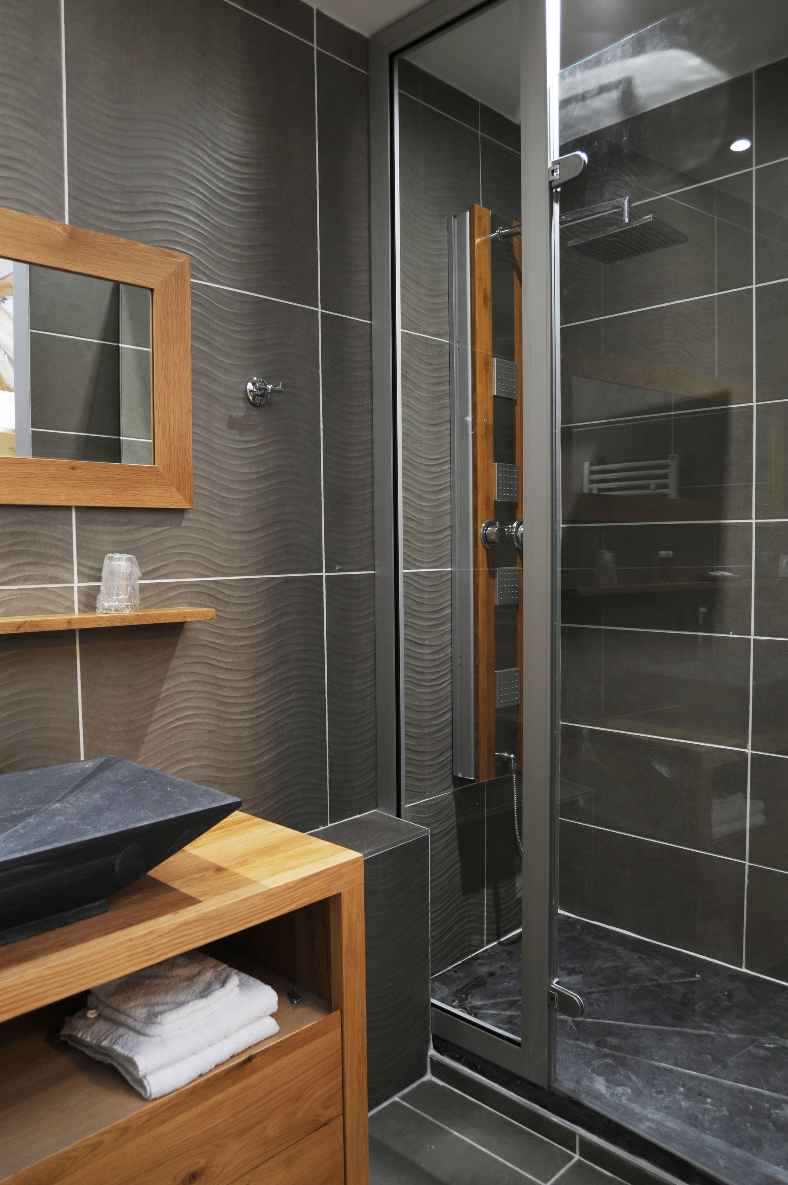A modern bathroom with a glass shower enclosure, a wooden vanity with a sink, and a mirror above it.