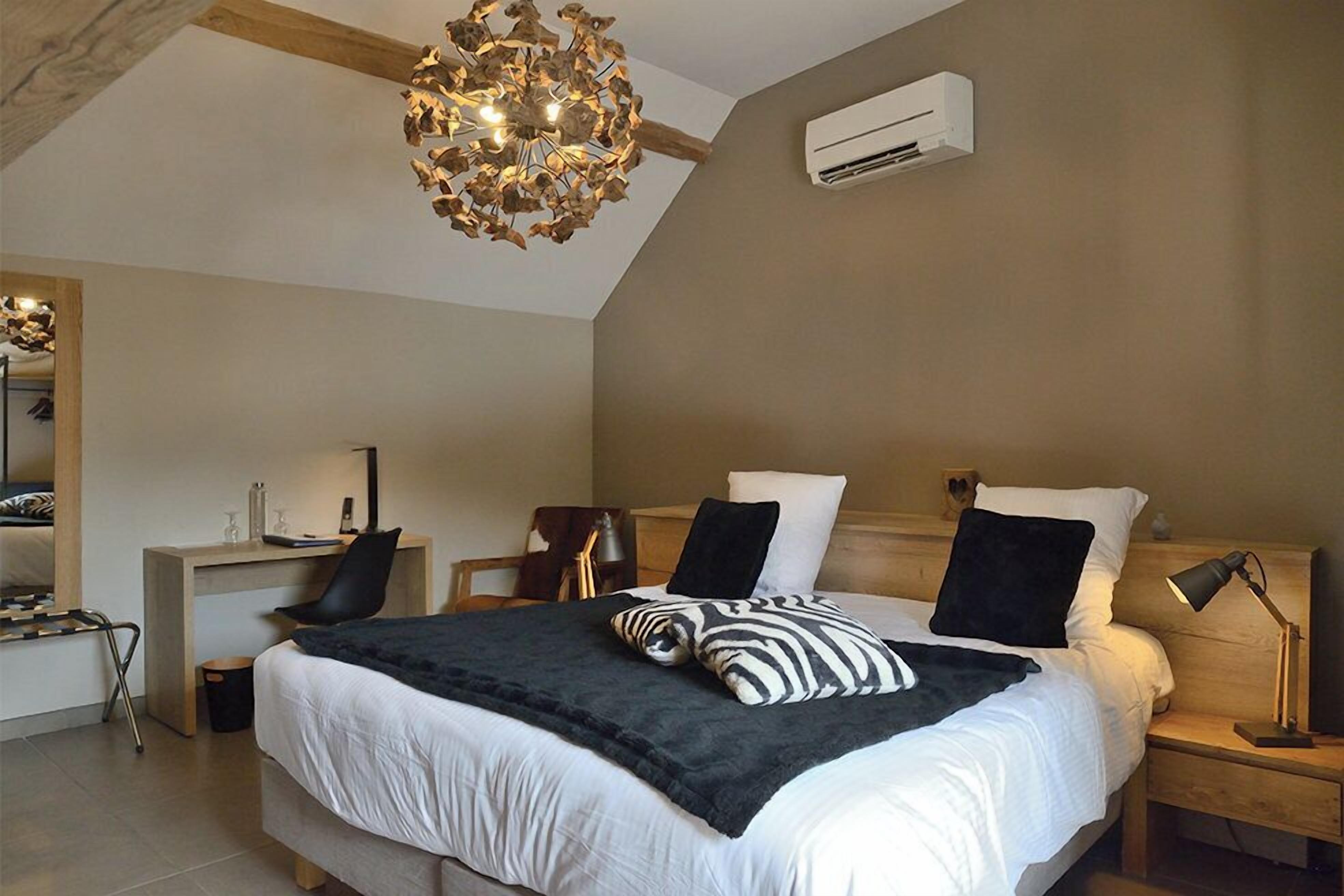 Een slaapkamer met een groot bed, een bureau, een stoel, een hanglamp en een airconditioner.