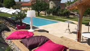 Zona de piscina con sillones de descanso, una lámpara y un edificio de piedra al fondo.