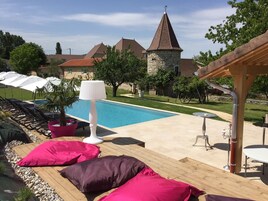 Un espace aménagé au bord de la piscine, avec des chaises longues, une lampe et un bâtiment en pierre en arrière-plan.