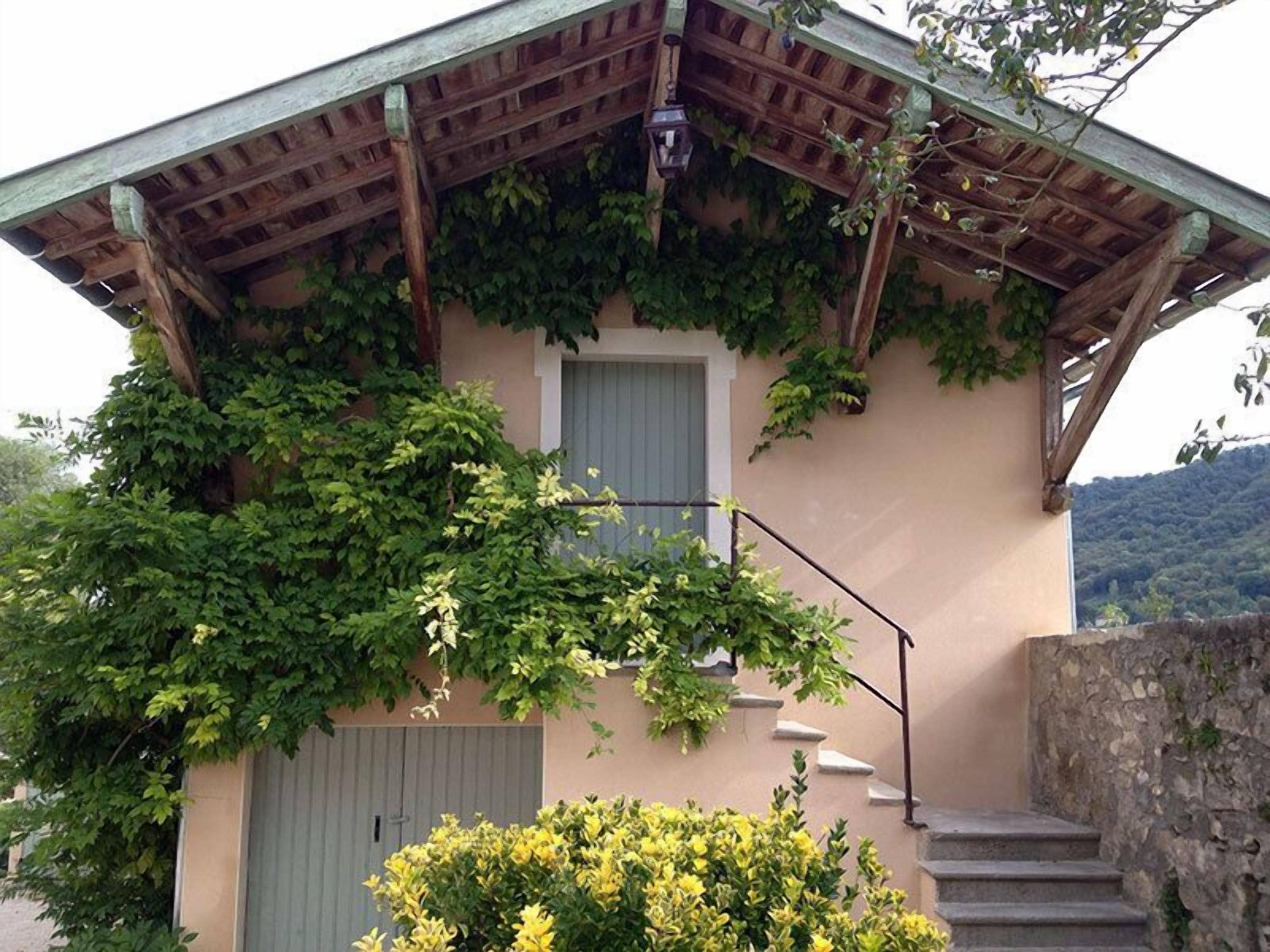 Un edificio con techo de pérgola de madera, una puerta verde y una escalera que lleva a un balcón.