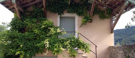 Un edificio con techo de pérgola de madera, una puerta verde y una escalera que lleva a un balcón.