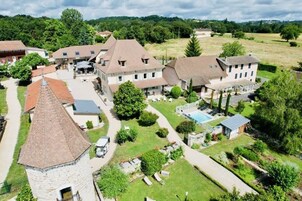 Un vaste domaine comprenant plusieurs bâtiments, dont une tour imposante, entouré d’une végétation luxuriante et doté d’une piscine.