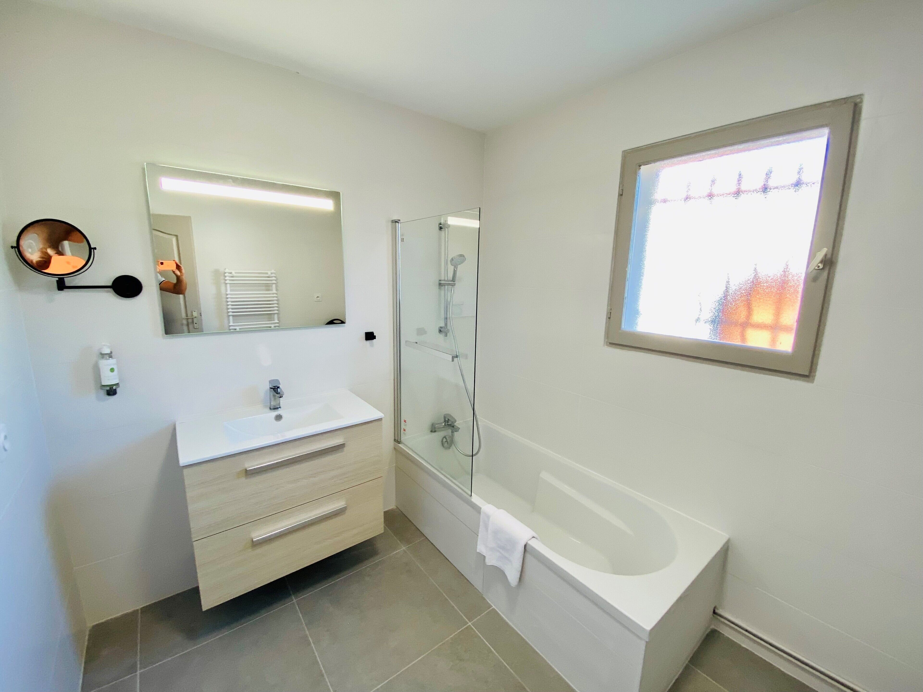 A modern bathroom with a white vanity, a large mirror, a glass-enclosed shower, and a bathtub.
