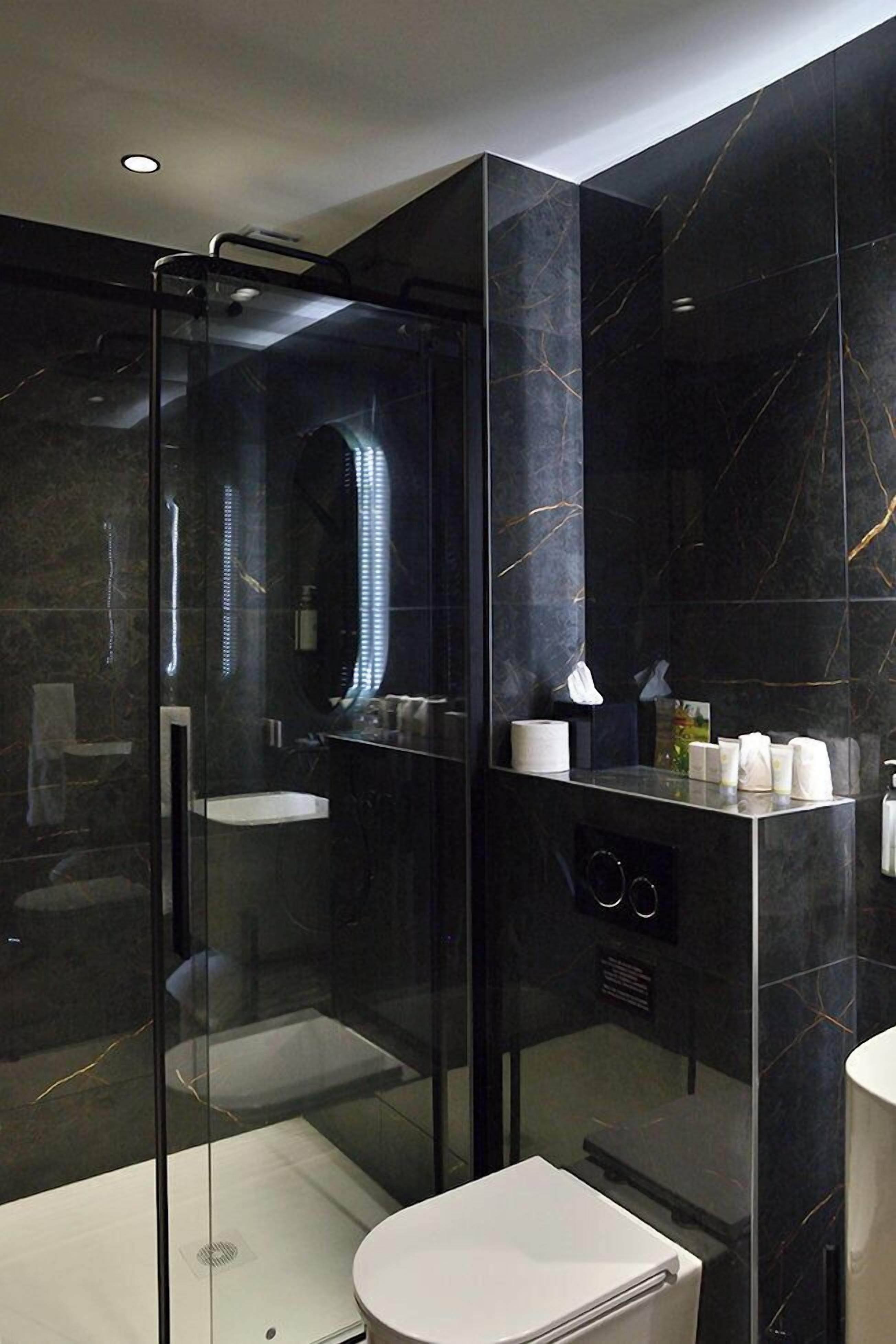 Un baño moderno con ducha envuelta en vidrio, inodoro blanco y pared revestida de mármol.