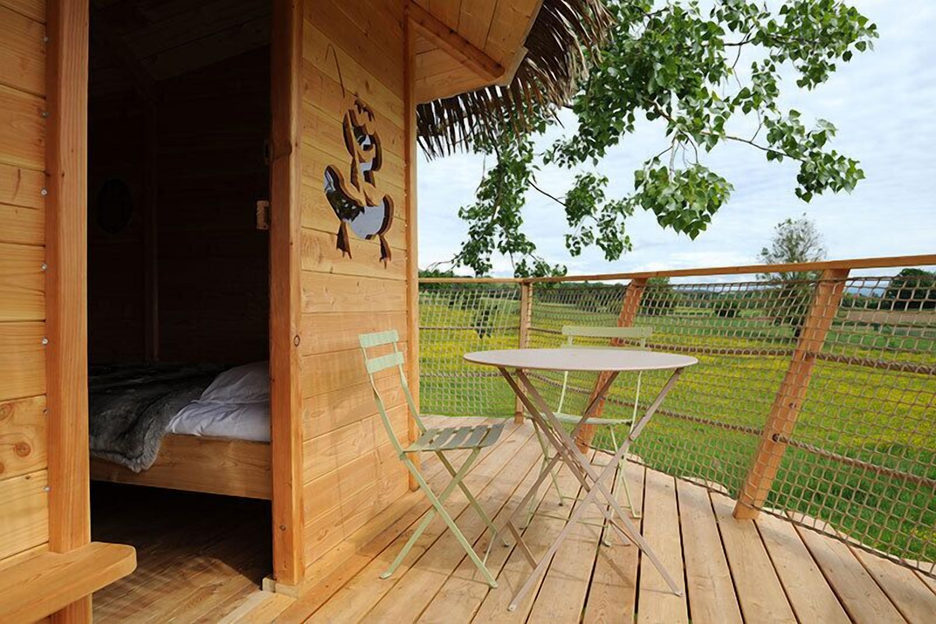 A wooden cabin with a bed, a table, and chairs on a deck.