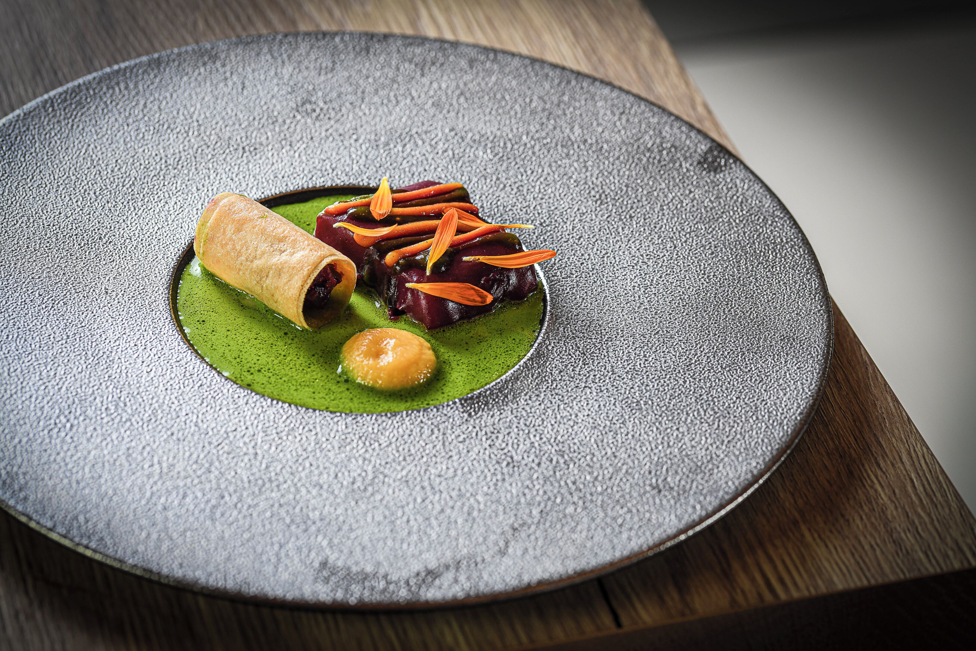 Un plato con un alimento enrollado, vegetales cortados y una salsa verde.