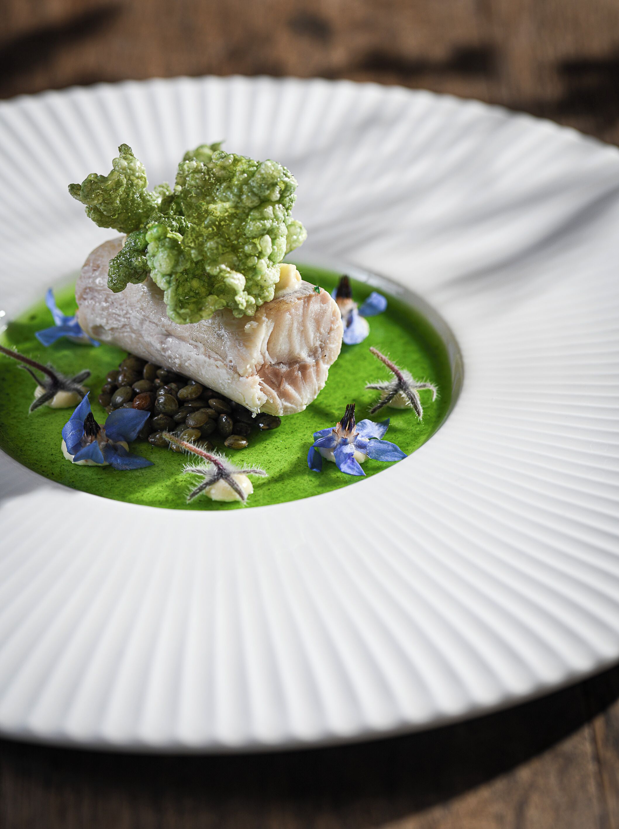 A white plate with a green sauce, a piece of fish, and decorative elements.