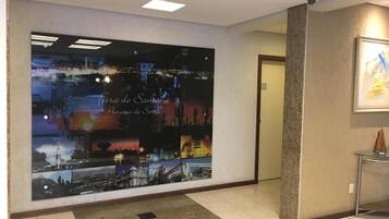 A hotel lobby with a large wall mural depicting a cityscape, a reception desk, and a framed artwork on the wall.