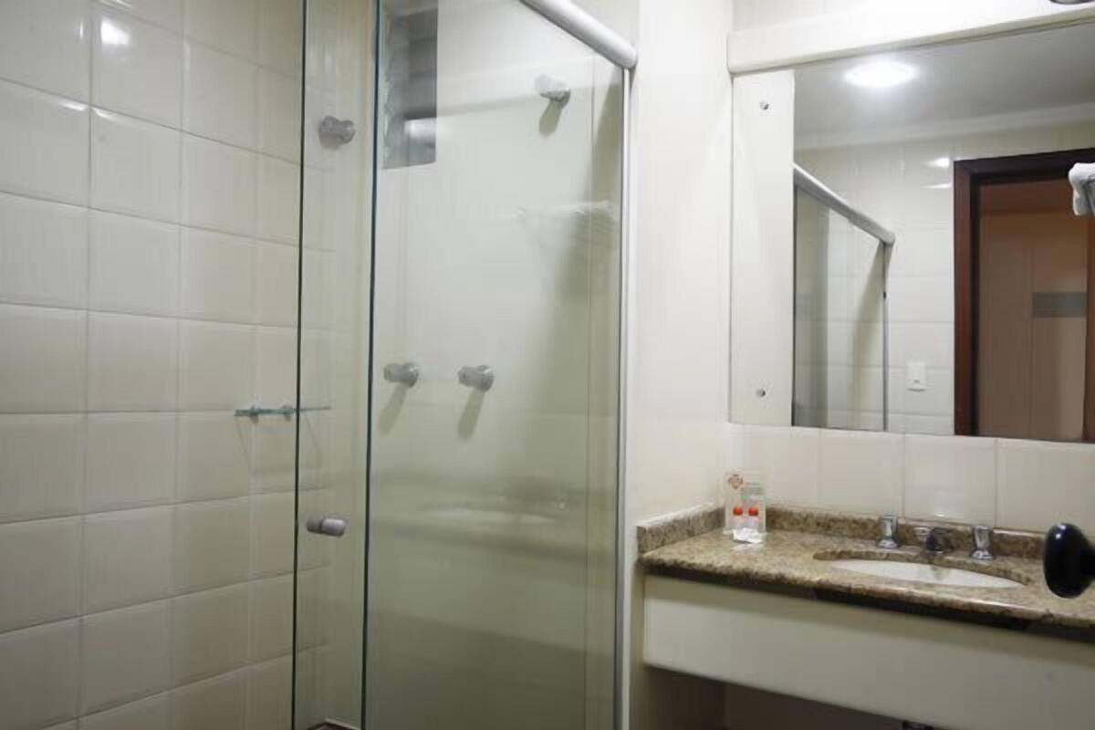 A bathroom with a glass shower enclosure, a sink with a granite countertop, and a mirror above the sink.