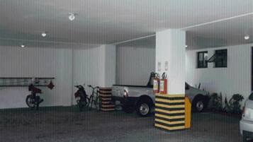 Un estacionamiento con una motocicleta, una bicicleta y un automóvil estacionados. Hay extintores y una manguera contra incendios en la pared.