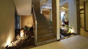 A modern interior with a staircase leading to a second floor, a small indoor garden, and a reception area. - Portal da Princesa Hotel (Feira de Santana)