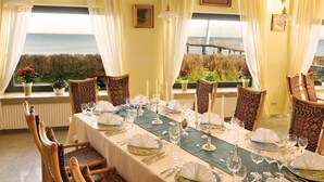 Un comedor con una mesa dispuesta para una comida, sillas y vistas al mar a través de amplias ventanas.