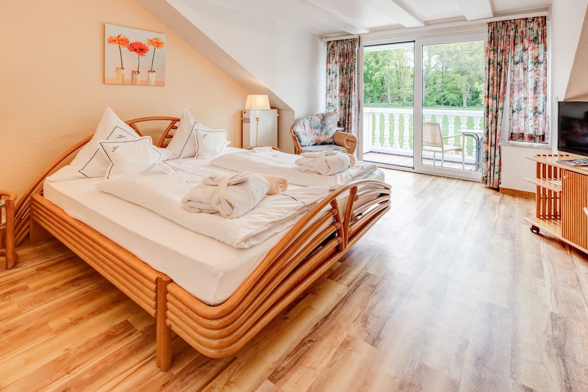 A bedroom with a wooden bed, a chair, a TV, and a balcony with curtains.