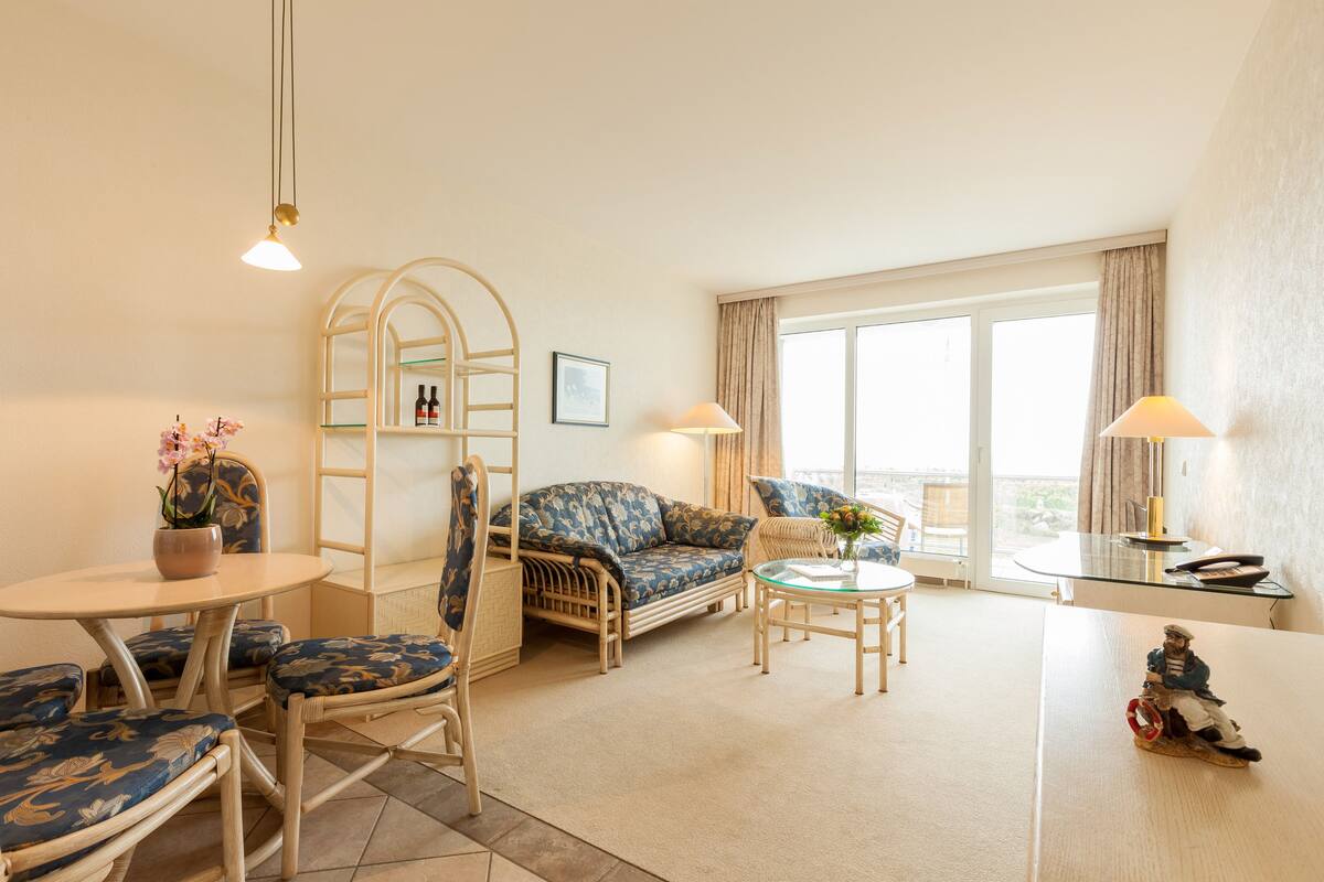 A cozy living room with a sofa, chairs, a small table, and a balcony with curtains.