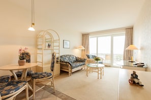 A cozy living room with a sofa, chairs, a small table, and a balcony with curtains. - Hotel Seeschlösschen (Hohwacht)