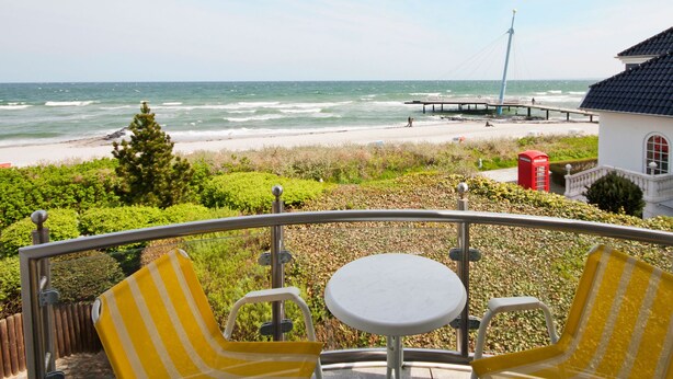 Un balcón con vista a la playa y al muelle, con una mesa y dos sillas a rayas.