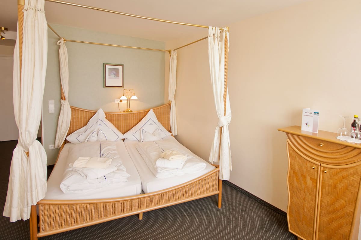 A four-poster canopy bed with white linens, a wicker headboard, and a bedside table with a lamp.