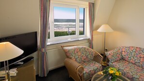 Habitación de hotel con televisión, una silla de mimbre, sofá, lámpara y ventana con vista al océano.