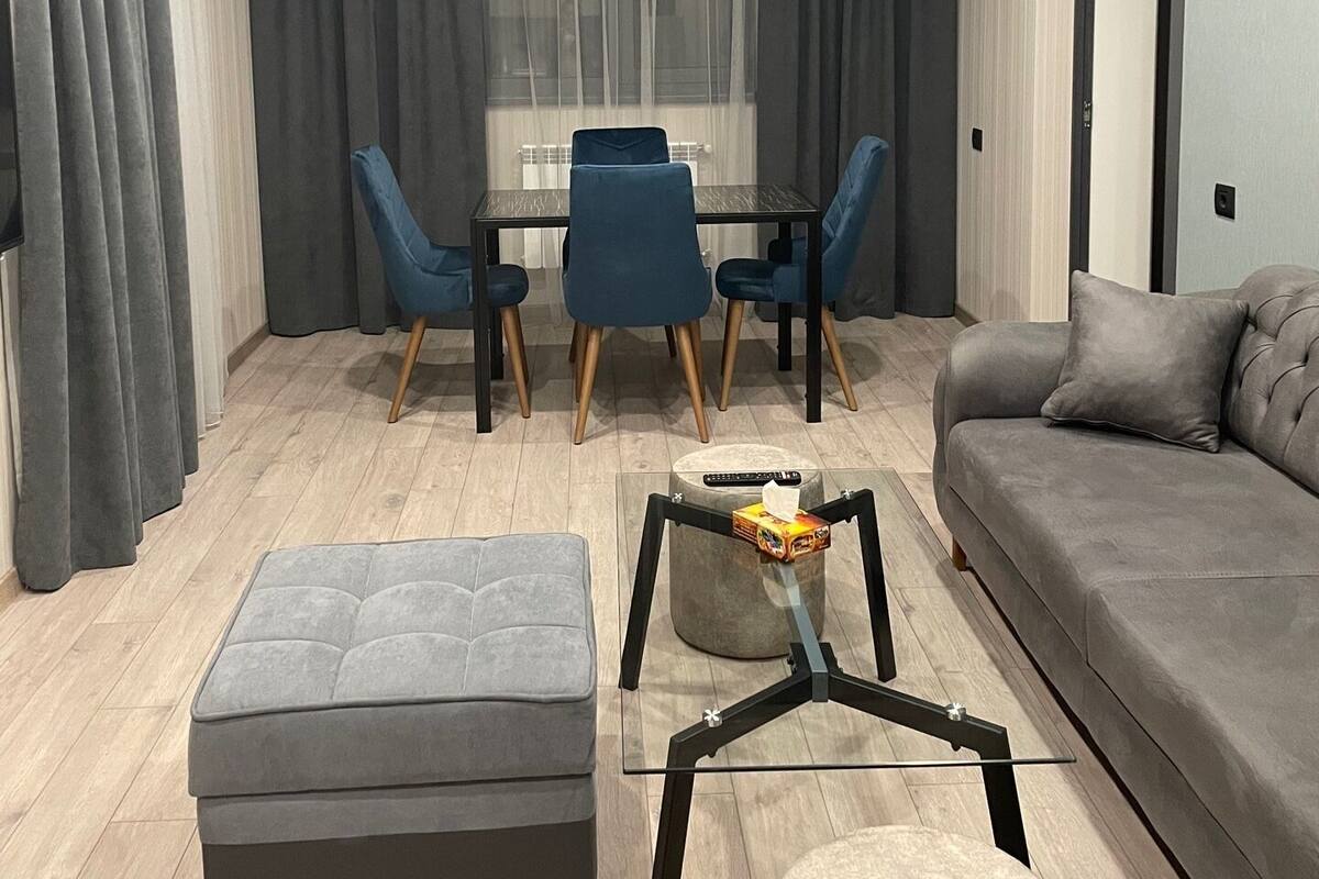 Ein modernes Wohnzimmer mit einem grauen Sofa, einem Glastisch und einem Essbereich mit Tisch und Stühlen.