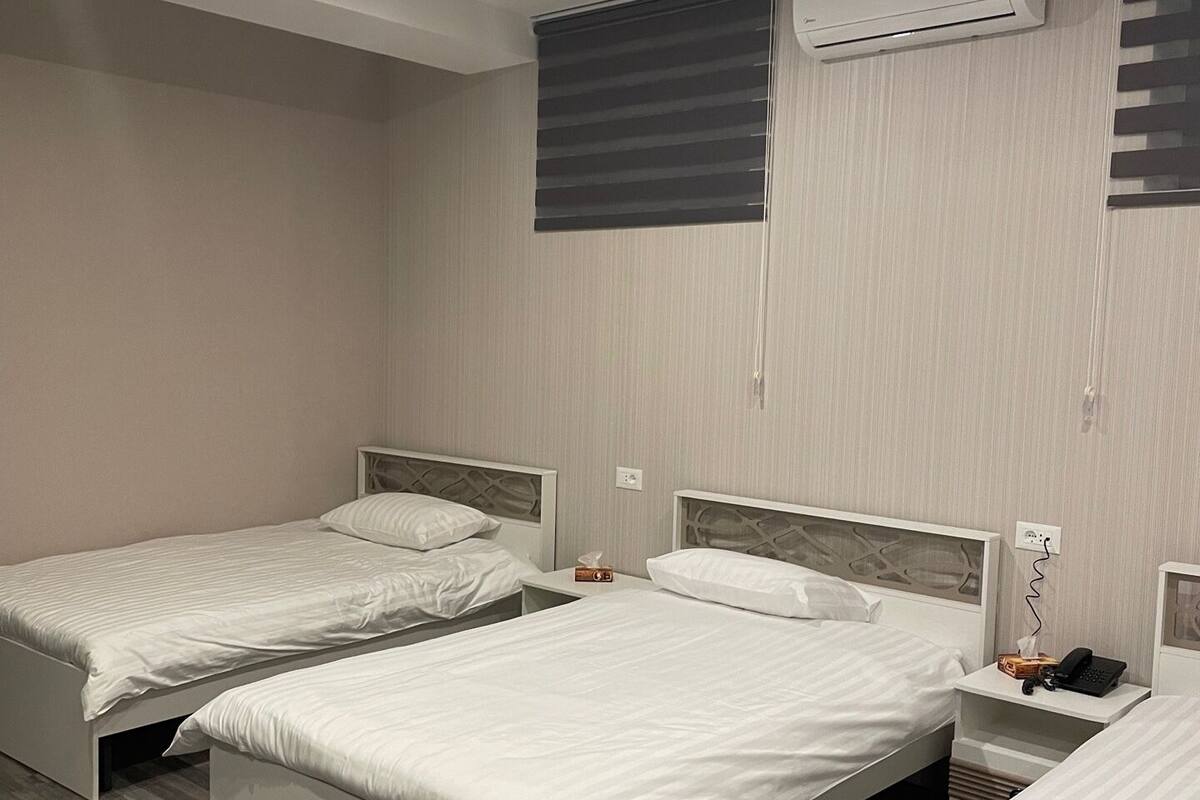 Ein Hotelzimmer mit drei Einzelbetten, einer Wandklimaanlage und einem Fenster mit Jalousien.