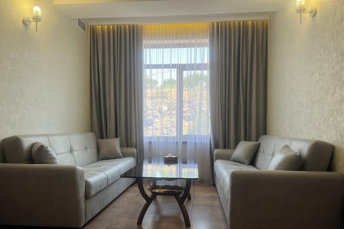 Ein Wohnzimmer mit zwei Sofas, einem Glastisch und einem großen Fenster mit Vorhängen.