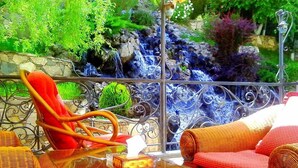 Un balcón con mobiliario de mimbre, una mesa de vidrio y vistas a una cascada.
