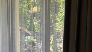 Una ventana con cortinas translúcidas, vista a un área boscosa y una estructura de piedra.