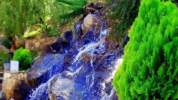 Una cascada fluye sobre rocas, con un muro de piedra y follaje verde.
