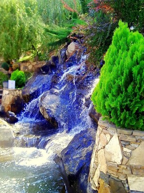 A waterfall cascading over rocks with a stone wall and green shrubbery. - Park Avenue Hotel (Yerevan)