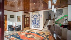 Un hall con techo de madera, alfombra estampada, un mostrador de recepción y una escalera con detalles en verde.