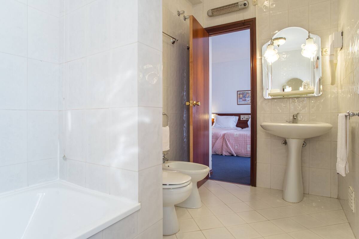 A bathroom with a bathtub, two toilets, a sink, and a mirror.