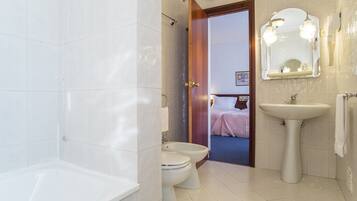 A bathroom with a bathtub, two toilets, a sink, and a mirror.