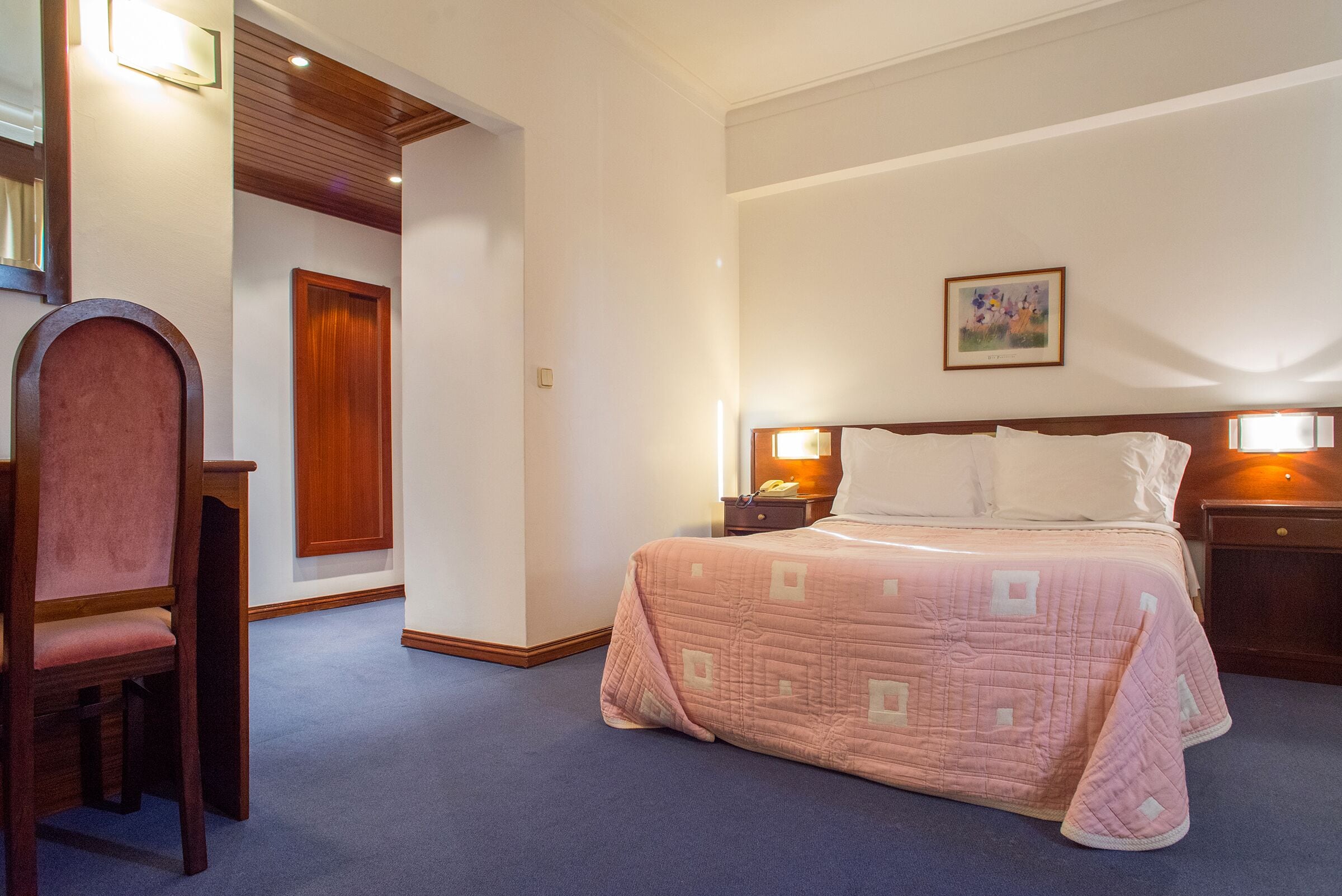 Una habitación de hotel con una cama, una silla, una mesita de noche y una puerta.