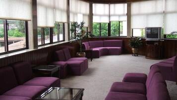 A room with a curved purple sofa set, a glass coffee table, and a television on a wooden stand.