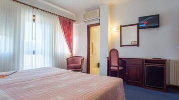 Habitación de hotel con una cama grande, un escritorio con una silla, televisión y ventana con cortinas.