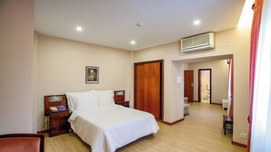 Una habitación de hotel con cama, mesita de noche, lámpara y una puerta que da al baño.