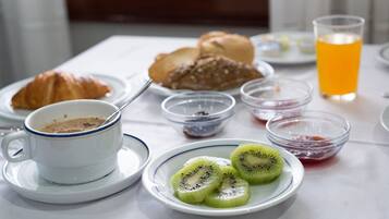 A breakfast setting with a croissant, kiwi slices, a cup of coffee, and a glass of orange juice on a table.