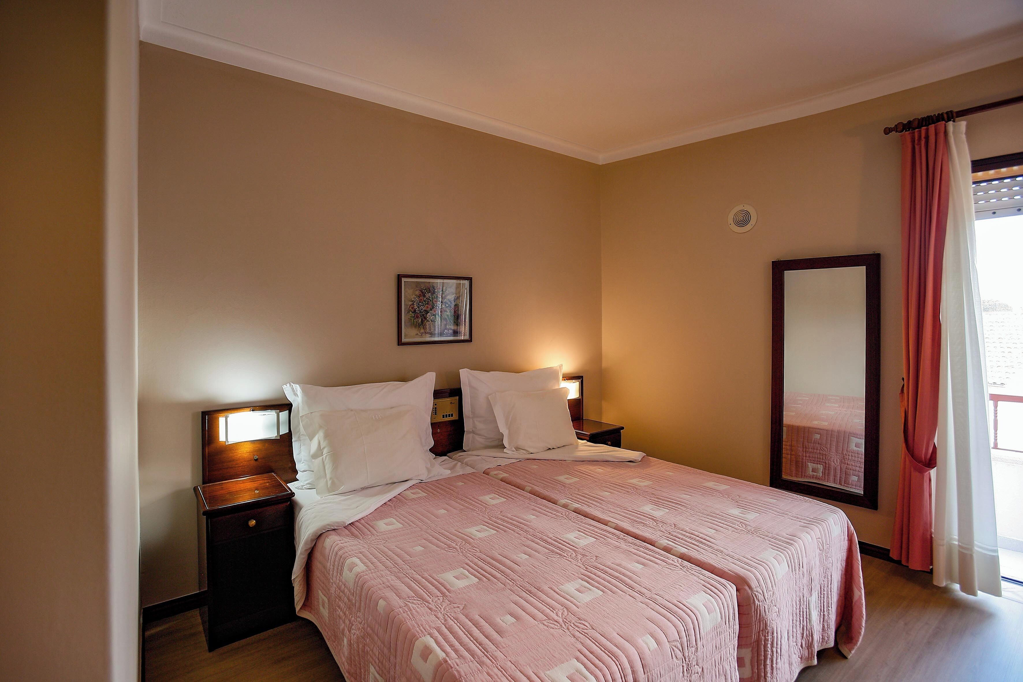 Un dormitorio con una cama grande, dos mesitas de noche, un tocador, un espejo y una ventana con cortinas.
