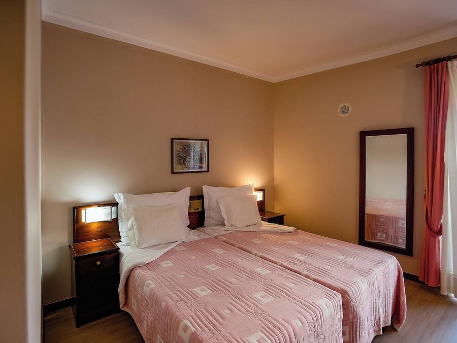 Un dormitorio con una cama grande, dos mesitas de noche, un tocador, un espejo y una ventana con cortinas.