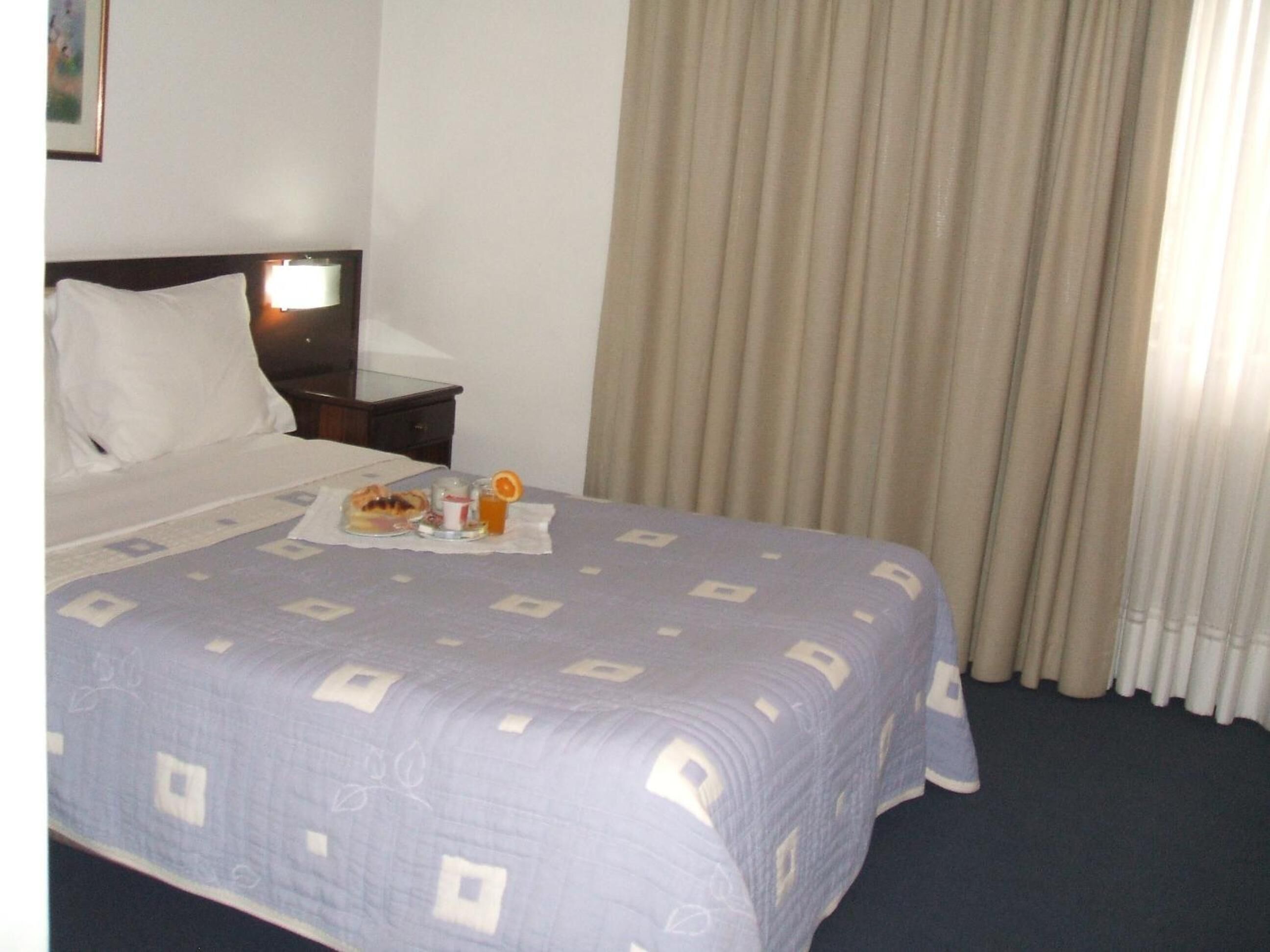 Una camera d'albergo con un letto, un comodino e un vassoio con prodotti per la colazione.