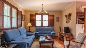 A living room with a blue sofa, a wooden coffee table, and a striped armchair. There is a chandelier, a fireplace, and a television.