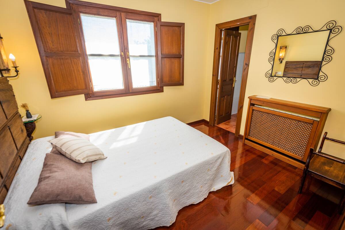 A bedroom with a bed, wooden wardrobe, and a window with open shutters.