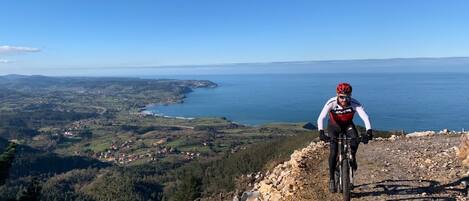 Ein Mountainbiker auf einem felsigen Weg mit einer schönen Aussicht auf eine Küstenlandschaft.